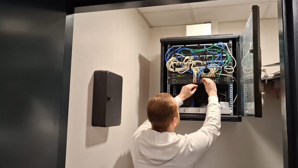 Mannelijke techneut bij een technische kast, symbool voor krachtig serverbeheer en professionele webhosting door een gespecialiseerd ICT‑bedrijf uit Gouda.