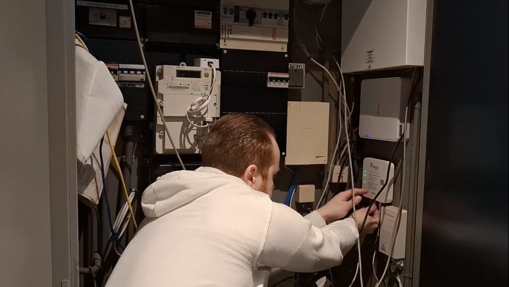 Mannelijke techneut aan het werk in een meterkast, bezig met het aanleggen en testen van glasvezel-, DSL- en back‑up internetverbindingen voor een stabiele netwerkinfrastructuur.