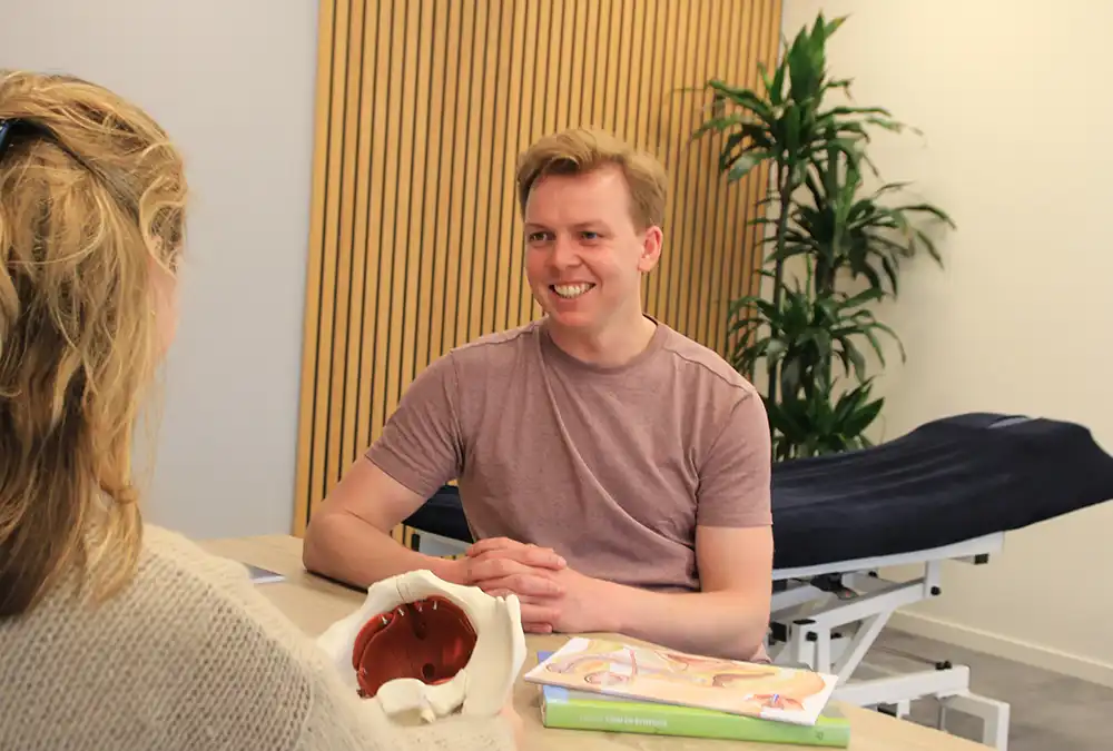 Therapeut in gesprek met cliënt in een moderne praktijkruimte.