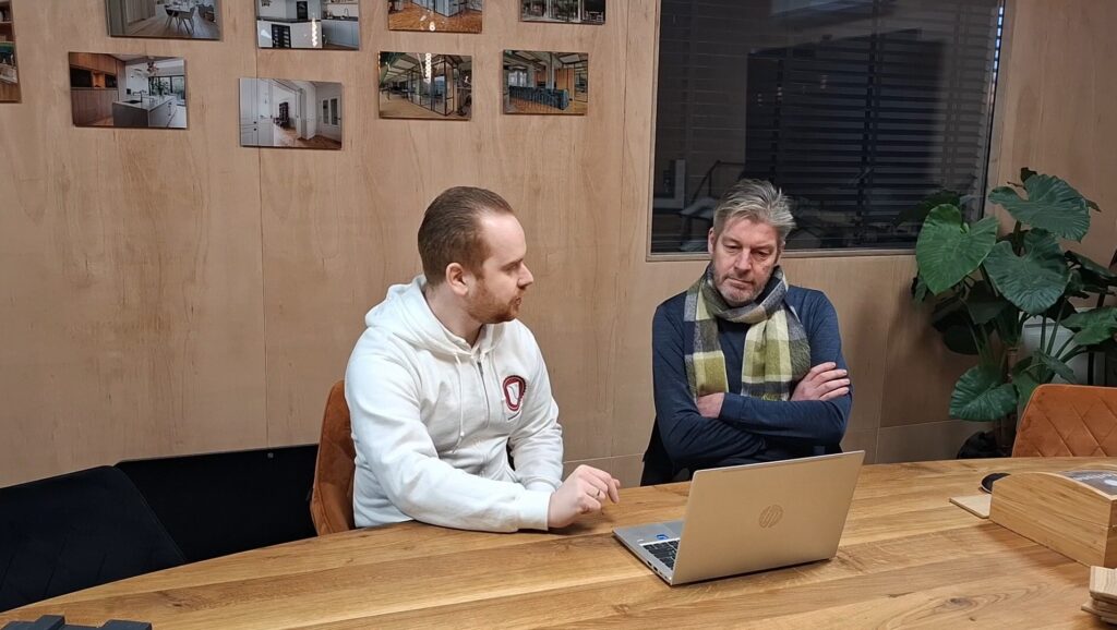 Consultant en klant in gesprek aan tafel met een laptop tijdens een cybersecurity‑adviesgesprek.